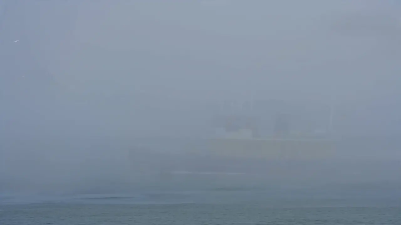 Een donker jacht komt langzaam uit dichte mist op de Noordzee tevoorschijn.